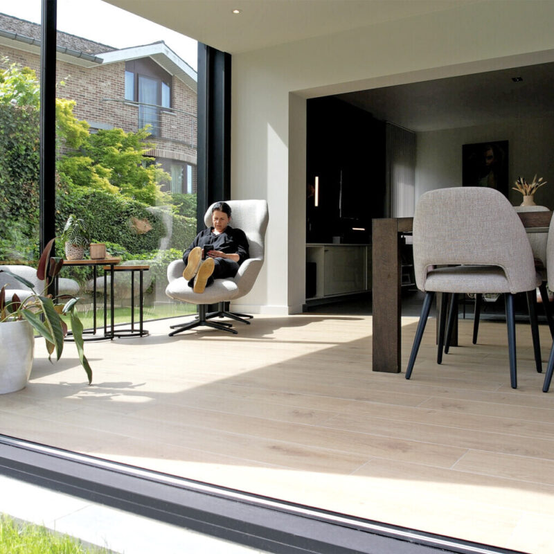 Moderne aanbouw veranda met dubbele schuifdeuren en houtlook vloerbekleding in Hoeilaart - Van Der Bauwhede