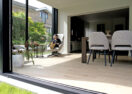 Moderne aanbouw veranda met dubbele schuifdeuren en houtlook vloerbekleding in Hoeilaart - Van Der Bauwhede